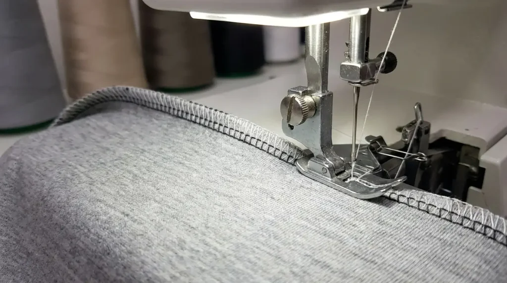Surjeteuse finissant le bord d'un tissu jersey gris avec une couture surfilée nette