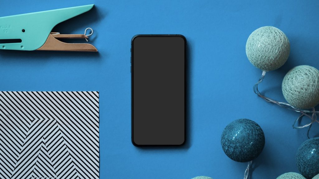 Téléphone à écran éteint posé à plat parmi des ciseaux et des pelotes de fil