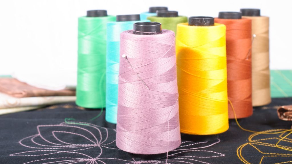 Cônes de fil pastel posés sur un tissu noir orné de motifs brodés à la machine