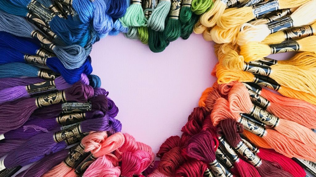 Échevettes de fil mouliné multicolores disposées en cœur sur fond rose