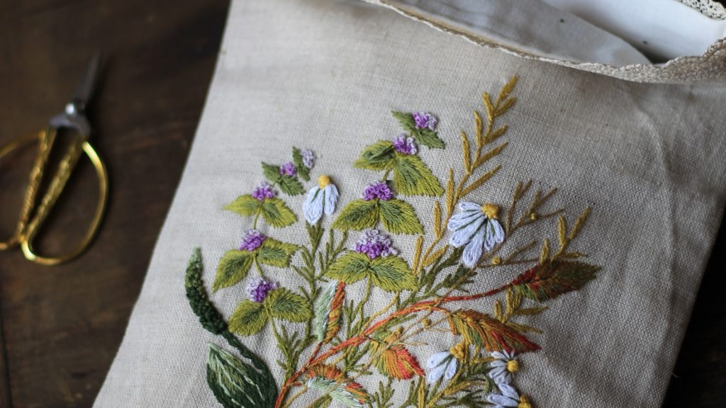 Motif floral brodé main sur du lin naturel, avec une paire de ciseaux dorés