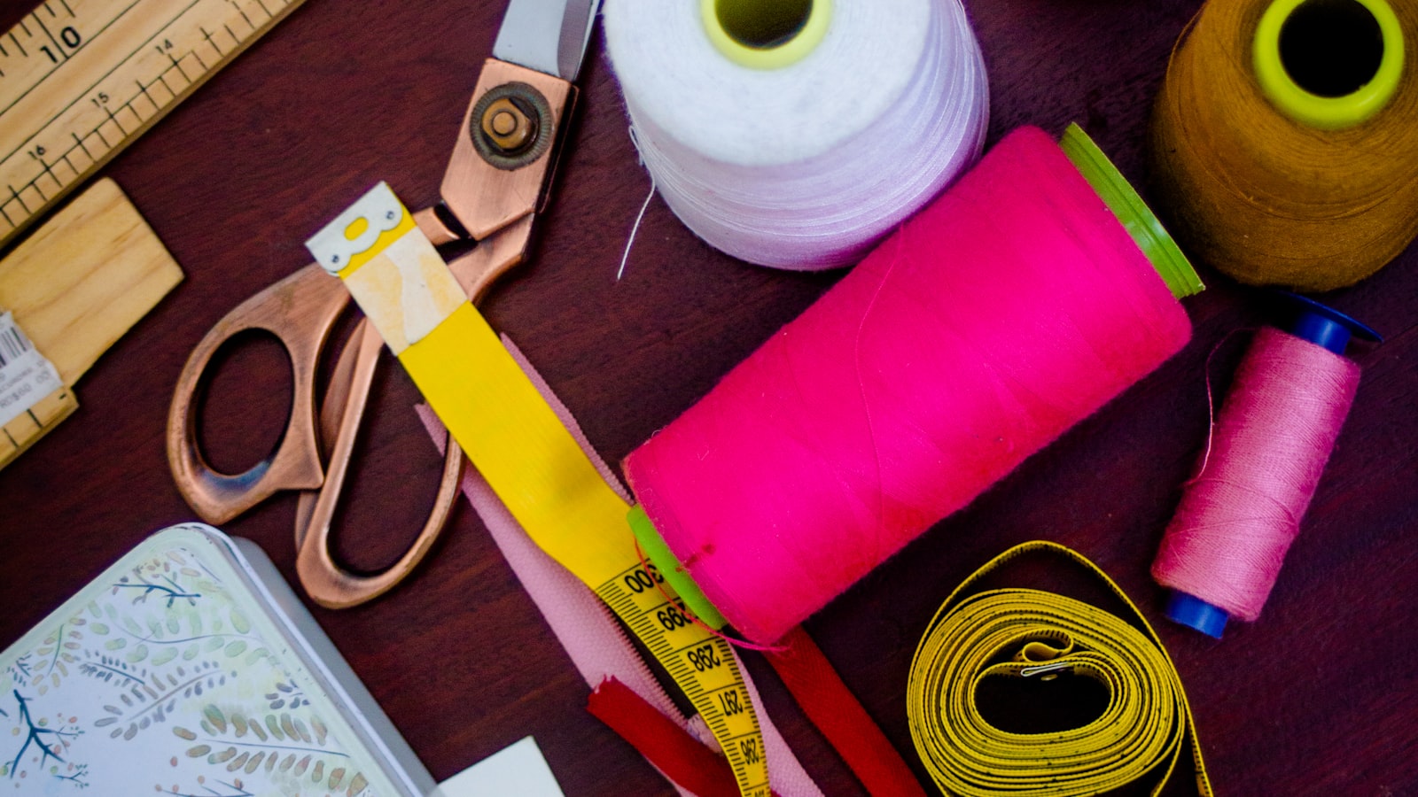 Matériel de couture coloré à plat : ciseaux de tailleur, bobines de fil, mètre ruban et rubans sur une table