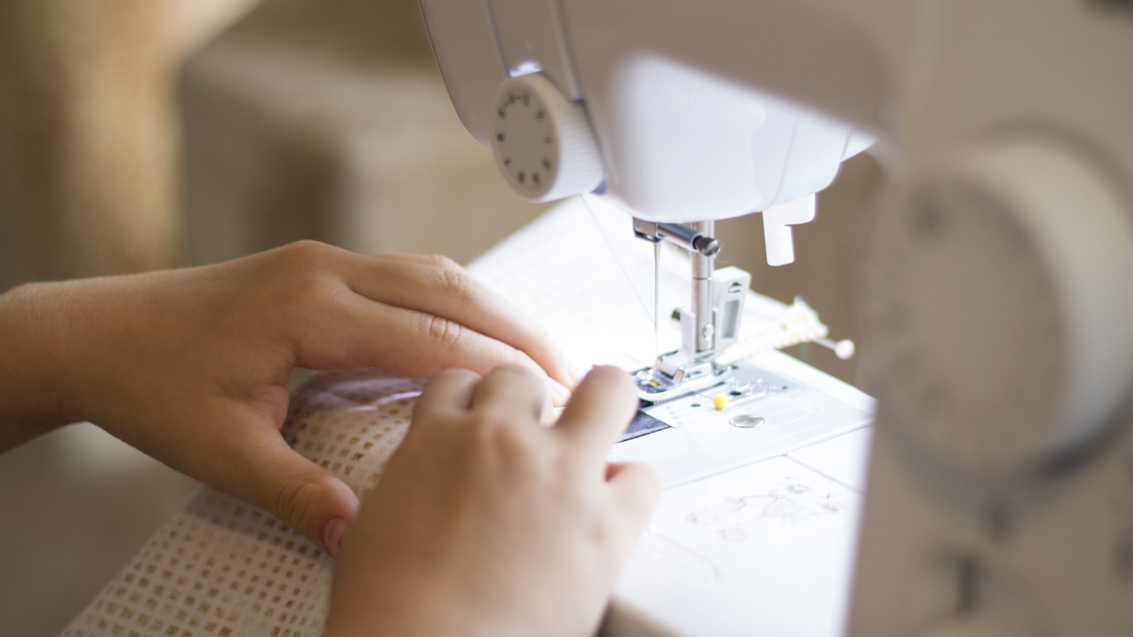 Mains guidant un tissu clair sous le pied-de-biche d'une machine à coudre blanche