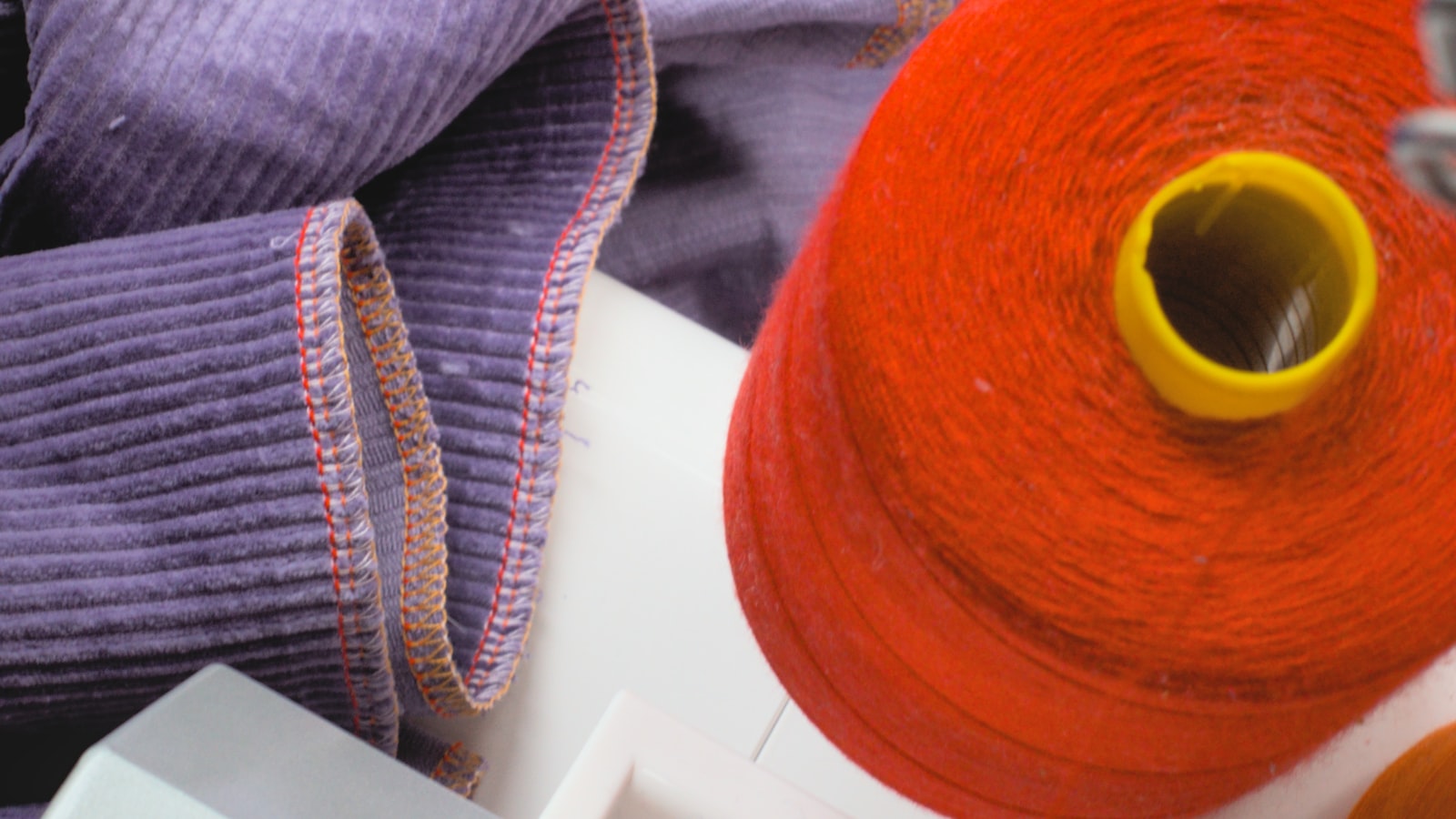 Bord de tissu velours surjeté avec des fils de couleurs différentes, à côté d'un cône de fil rouge