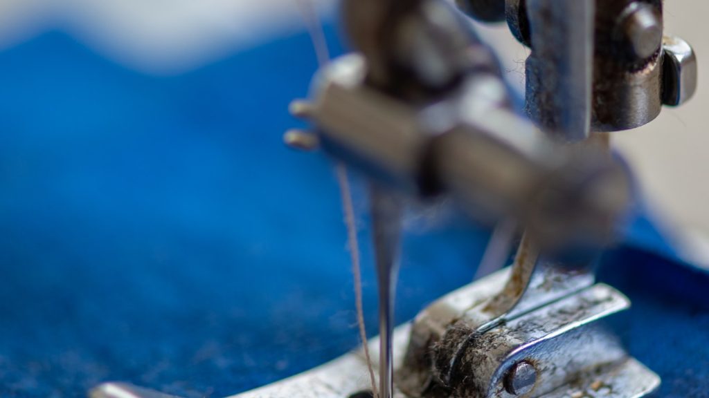 Gros plan du pied-de-biche et des fils d'une machine en train de coudre un tissu bleu